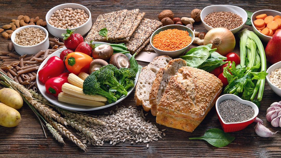 Kohlenhydratreiche Lebensmittel, unter anderem Brot, Nudeln, Obst und Gemüse, auf einem Holztisch