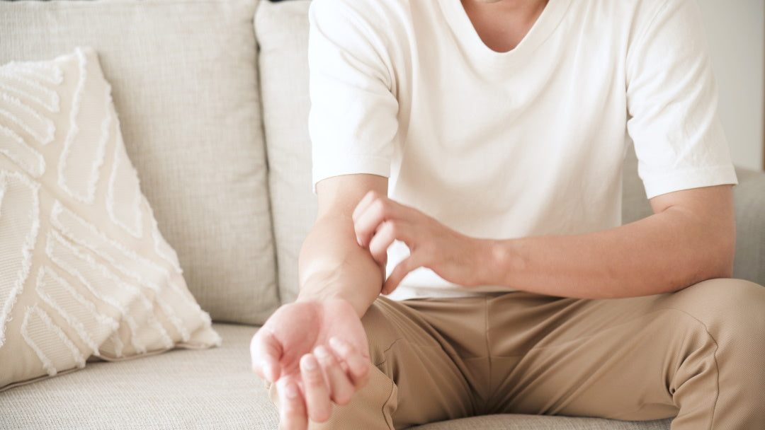 Mann sitzt auf dem Sofa und kratzt sich am Arm